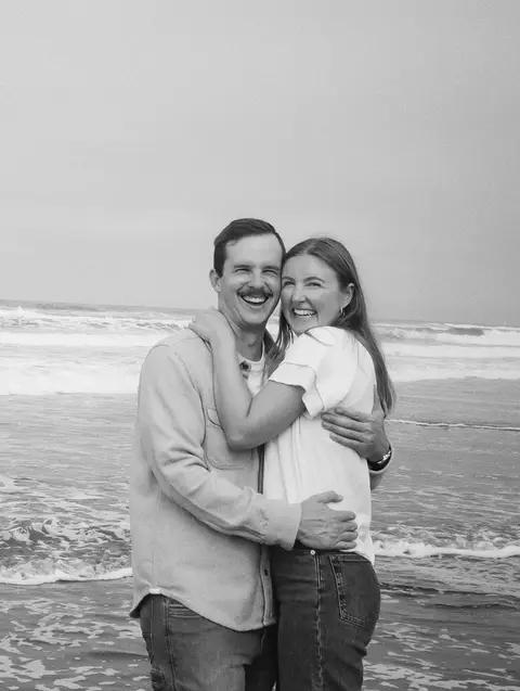 Black and white 35mm film engagement photo of a couple hugging and laughing at the edge of the surf on a foggy San Francisco beach.