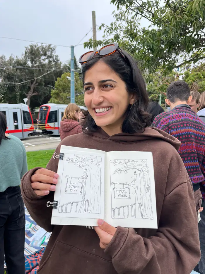 A smiling workshop participant holding up a sketchbook filled with line drawings.