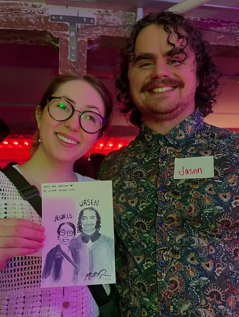 Two guests wearing name tags hold up their five-minute watercolor portrait at a neighborhood event