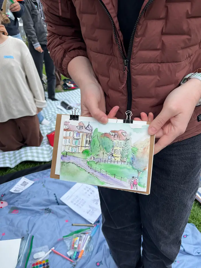 A participant holding open a sketchbook with a colorful watercolor painting of the park.