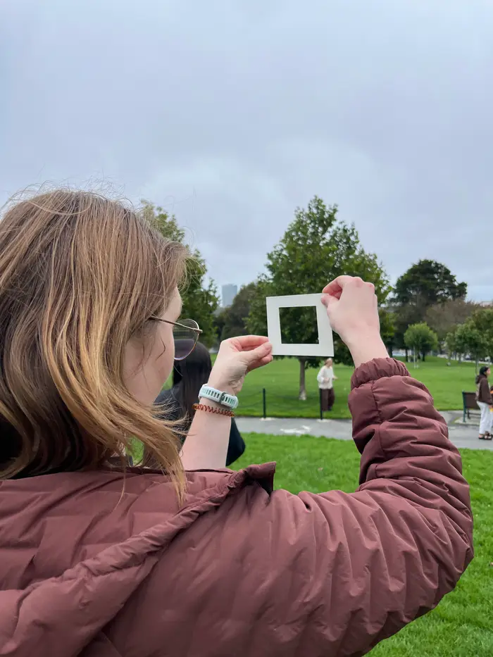 A workshop participant using a small viewfinder to frame a scene in the park.