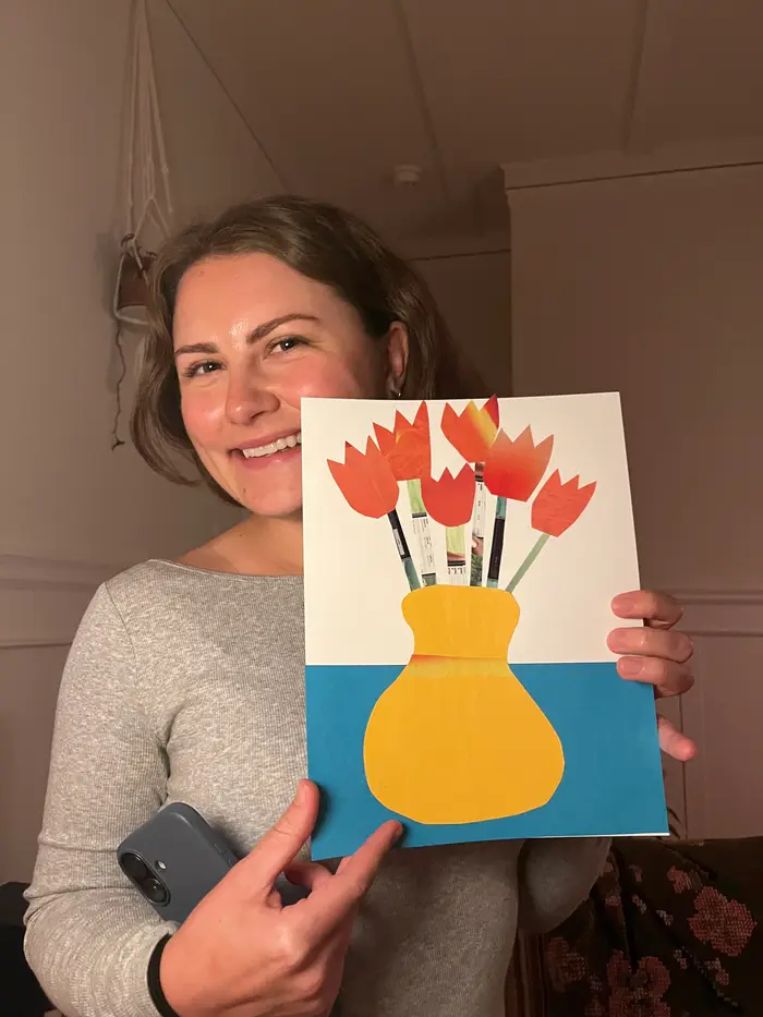 A smiling participant holding a collage of red tulips in a yellow vase.