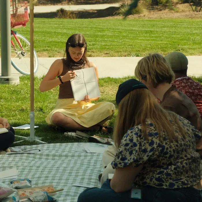 Natalie showing a sketchbook drawing to participants seated in the park.