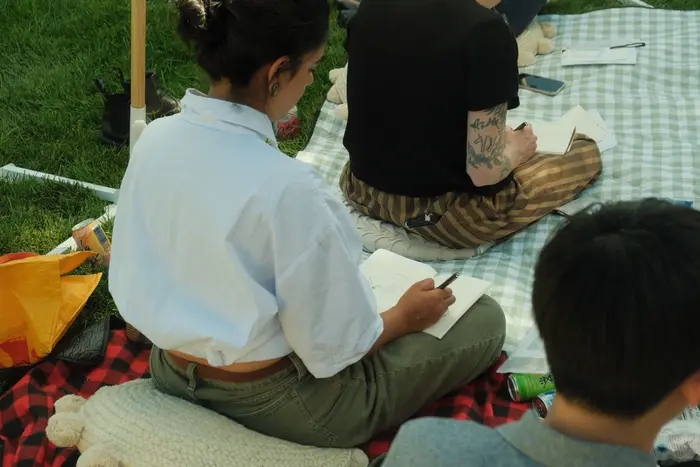 Workshop participants drawing in sketchbooks while sitting on picnic blankets.
