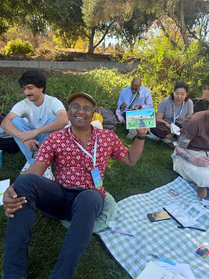 A smiling participant in a red patterned shirt holding up a painting of the park.