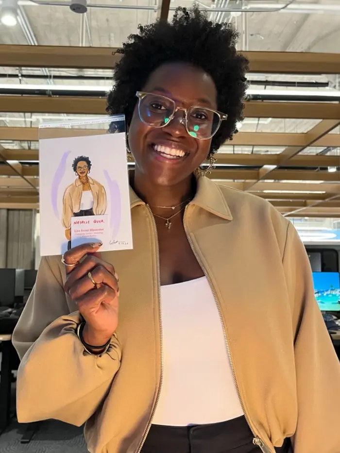 Smiling guest in glasses and a tan jacket holding her illustrated portrait